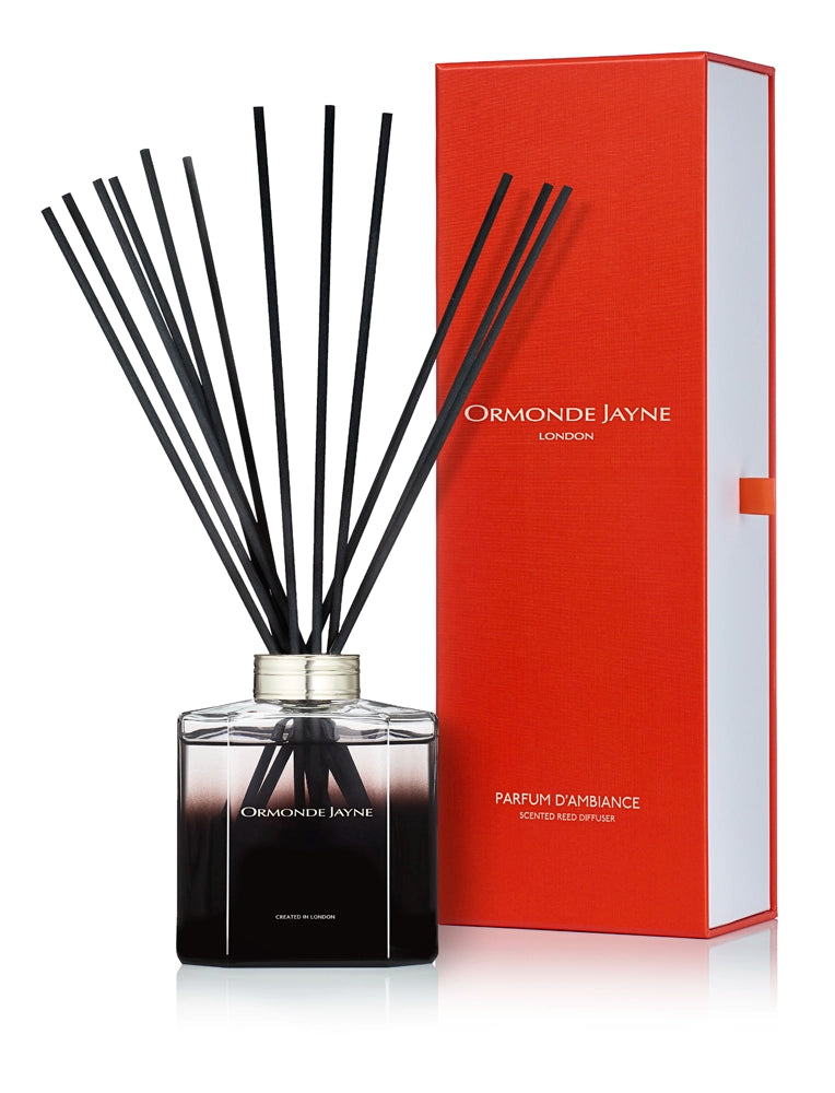 Black scented reed diffuser in glass bottle with silver cap and tall black reeds, beside red packaging box
