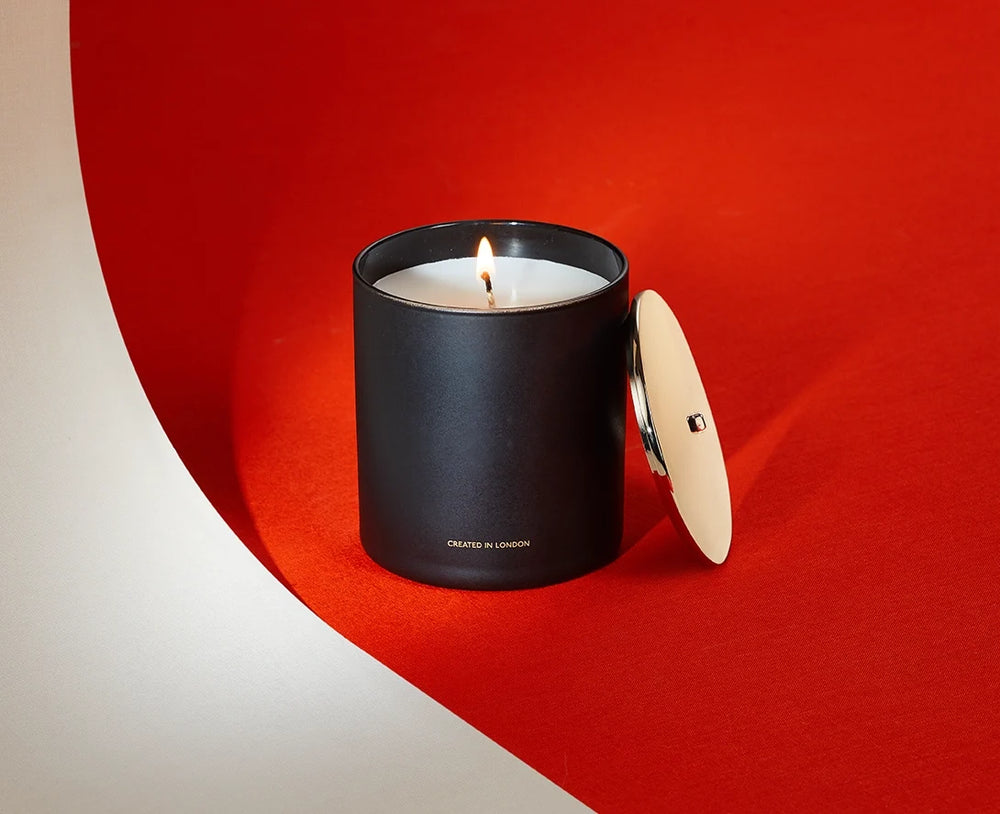 A black scented candle, lit, on vermilion
